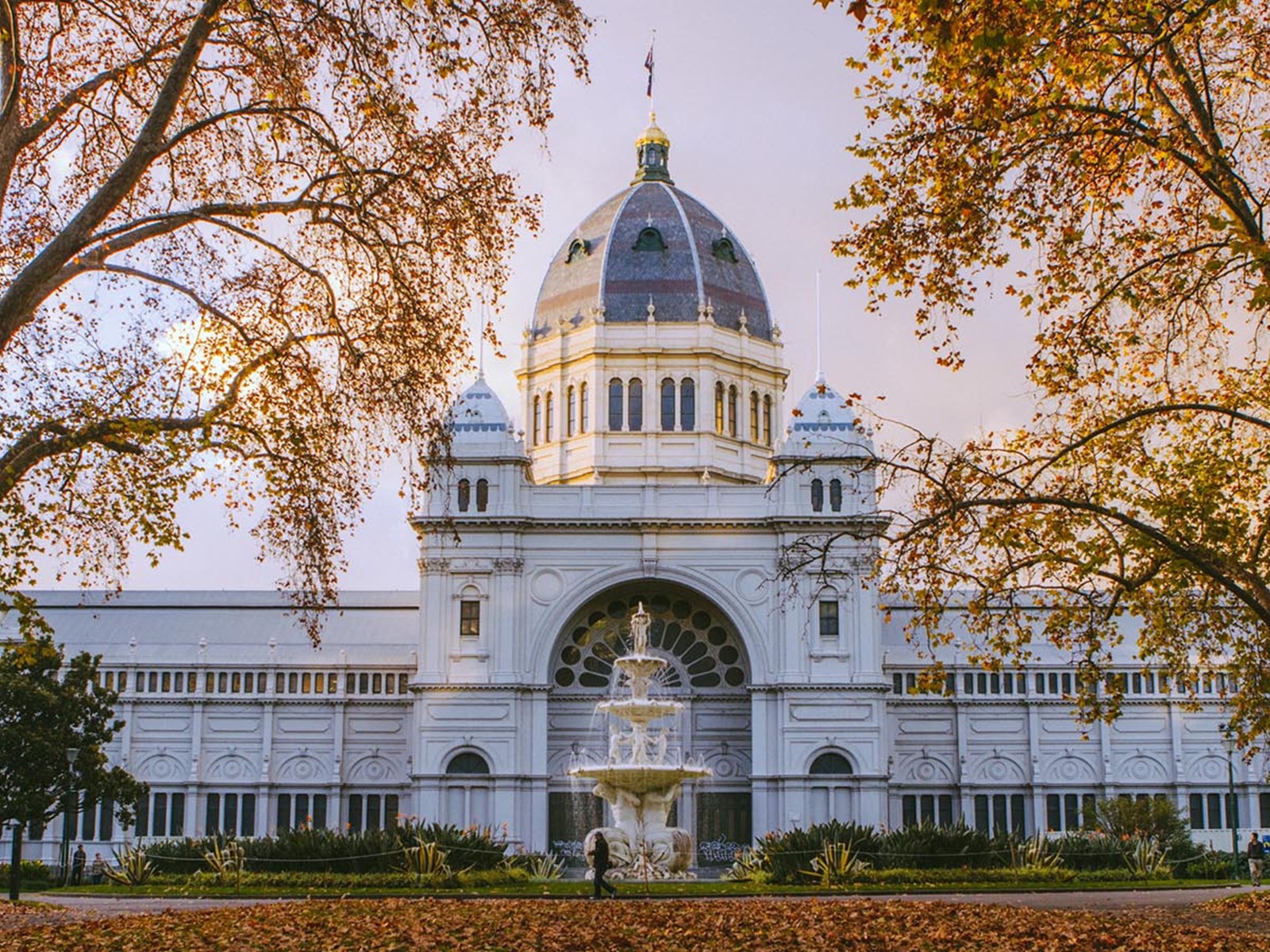 The grand Royal Exhibition Building framed by autumn trees and a fountain in front.
