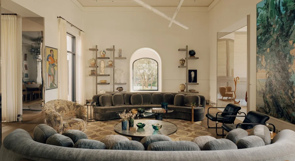 Spacious modern living room with neutral tones, curved grey sofas, low coffee tables, open wall shelving, and large artwork, best interior designers in Paris