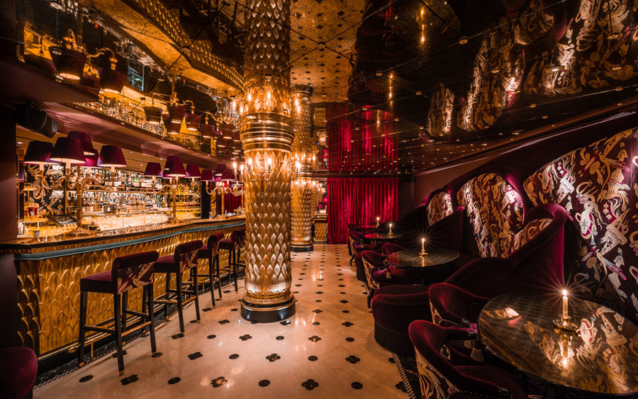 Opulent Asian-inspired bar featuring dark red velvet seating, golden scale-textured columns, polished marble floors, and warm, ambient lighting, best interior designers in Paris