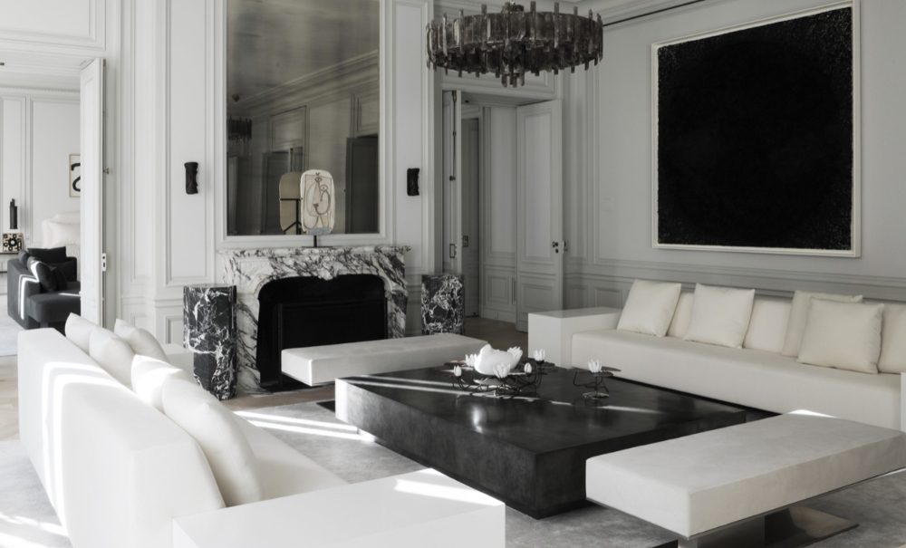 Bright living room blending traditional architecture with tropical elements, featuring an ornate stone fireplace, green foliage-patterned sofas, and a detailed coffered ceiling, best interior designers in Paris