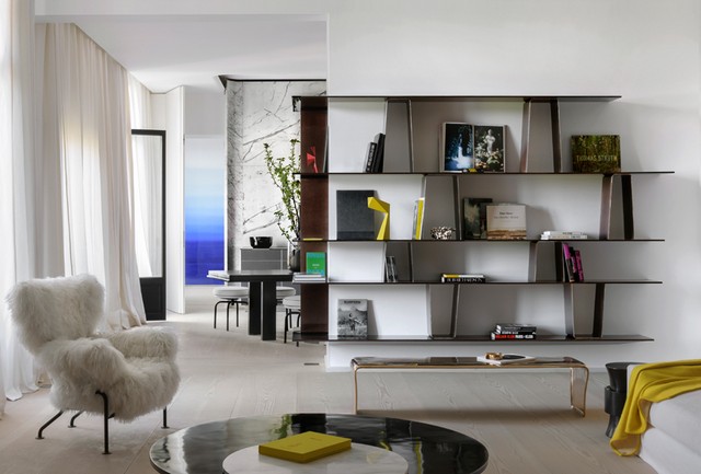Modern apartment interior featuring a white fluffy armchair, a sleek black-and-marble coffee table, light wooden floors, and a dark geometric open bookcase, best interior designers in Paris