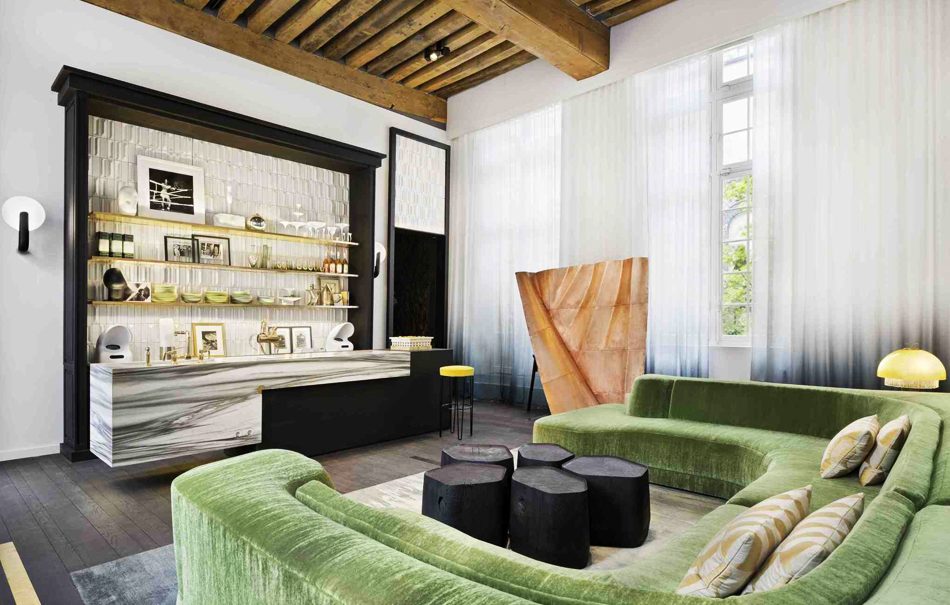 Contemporary interior featuring a large green sectional sofa, black wooden coffee tables, exposed ceiling beams, and a marble home bar setup, best interior designers in Paris