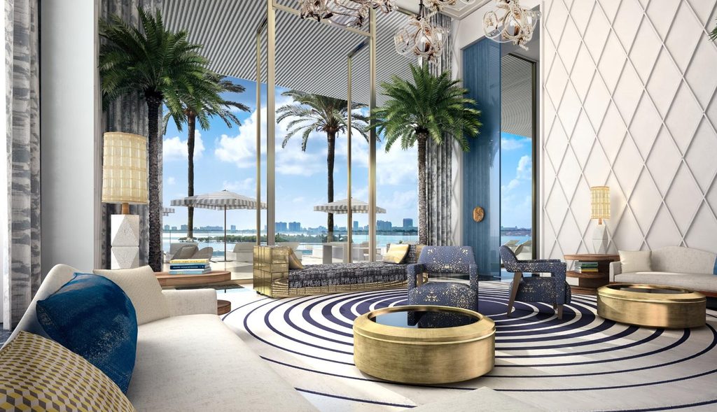Luxurious beachfront lounge with high ceilings, tropical palm trees indoors, golden coffee tables, blue patterned armchairs, and floor-to-ceiling ocean views, best interior designers in Paris