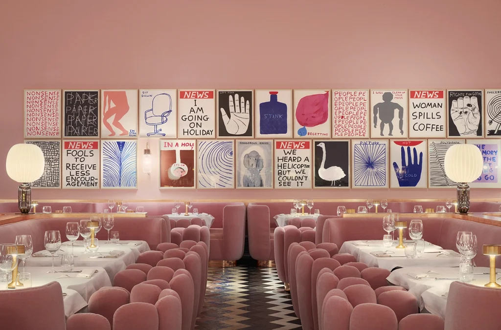 Monochromatic pink restaurant interior with plush velvet seating, small table lamps, and a wall gallery of framed typographic prints, best interior designers in Paris