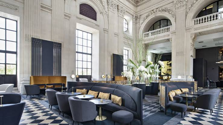 Grand, opulent dining room with massive crystal chandeliers hanging from an ornate gold ceiling, surrounded by high white columns and curved futuristic seating domes, best interior designers in Paris