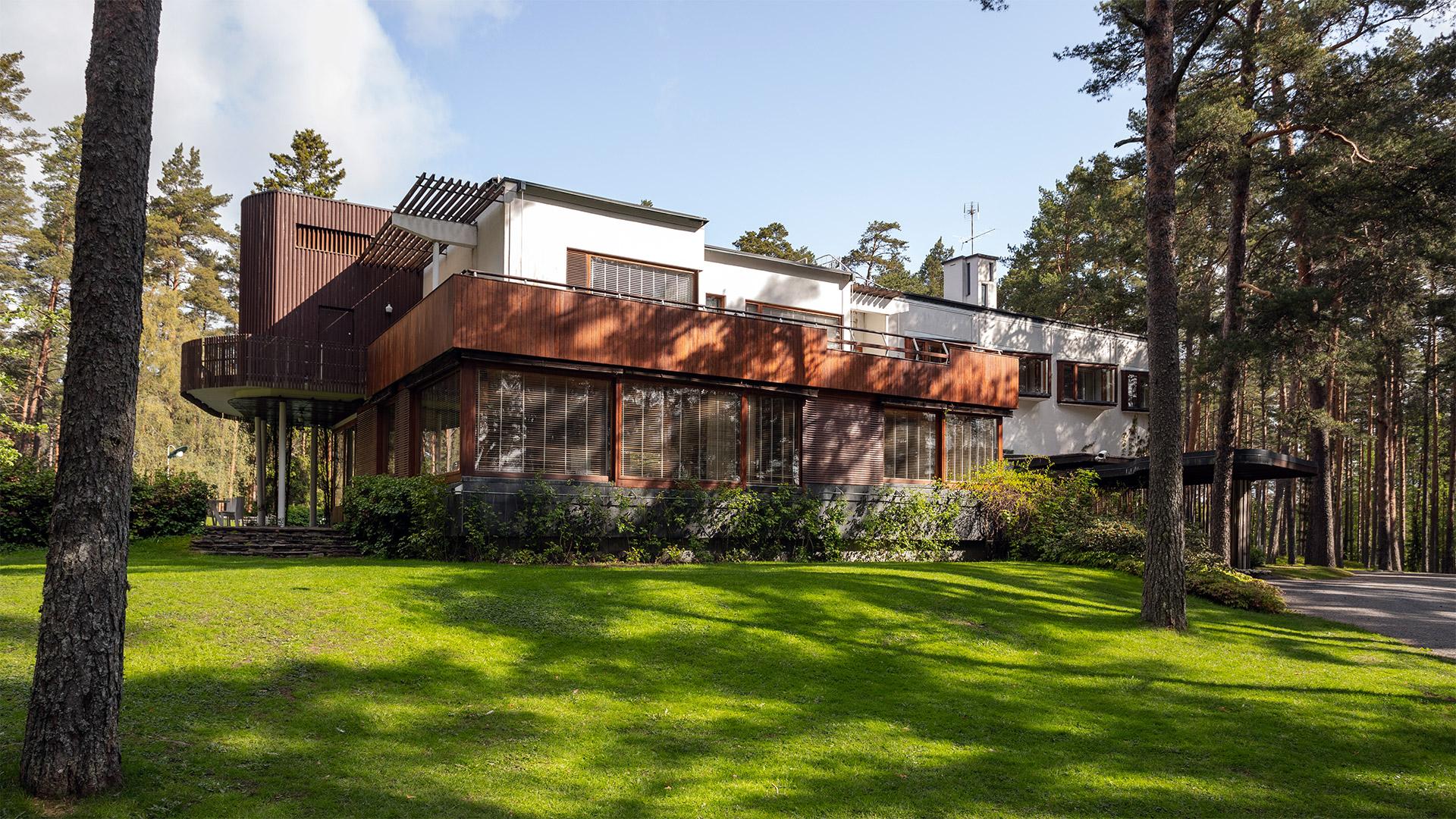 Modern home nestled in a pine forest featuring white plaster, dark wood cladding, and upper-level balconies.