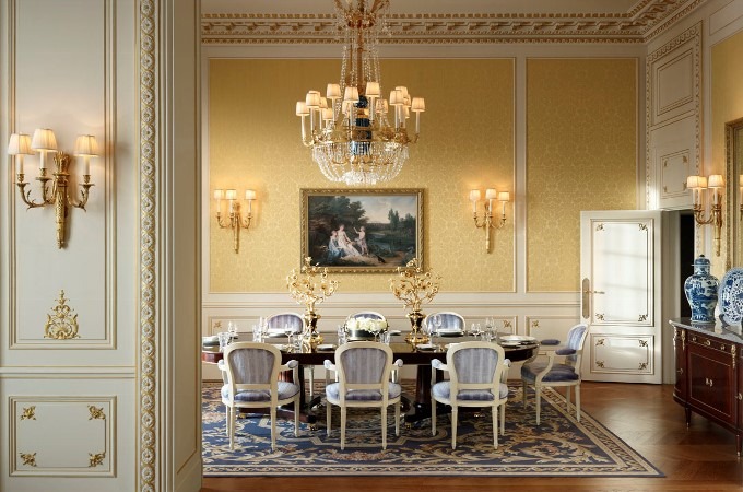 Formal dining room with classical gold moldings, yellow wall panels, a crystal chandelier, and a dark polished dining table with blue-upholstered chairs, best interior designers in Paris