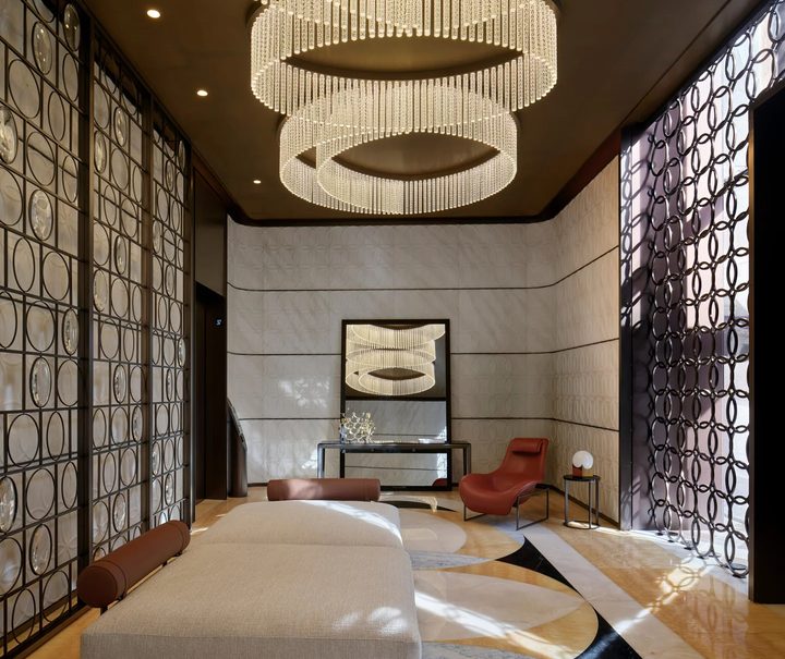 Grand entrance hall with polished marble floors, an elaborate layered ring chandelier, and a low cream daybed top interior design firms in milan
