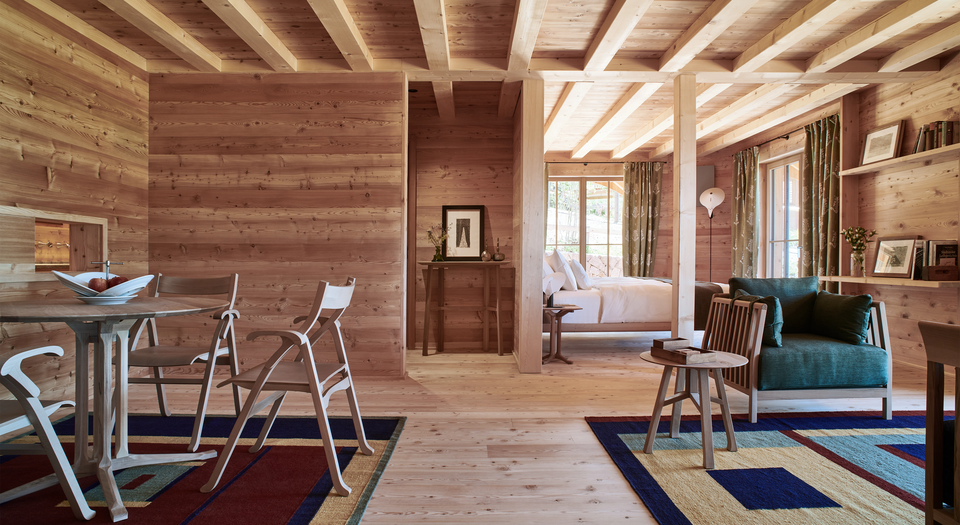 Alpine-inspired interior clad entirely in light wood paneled walls and ceilings, with a small dining set and cozy armchair. top interior design firms in milan