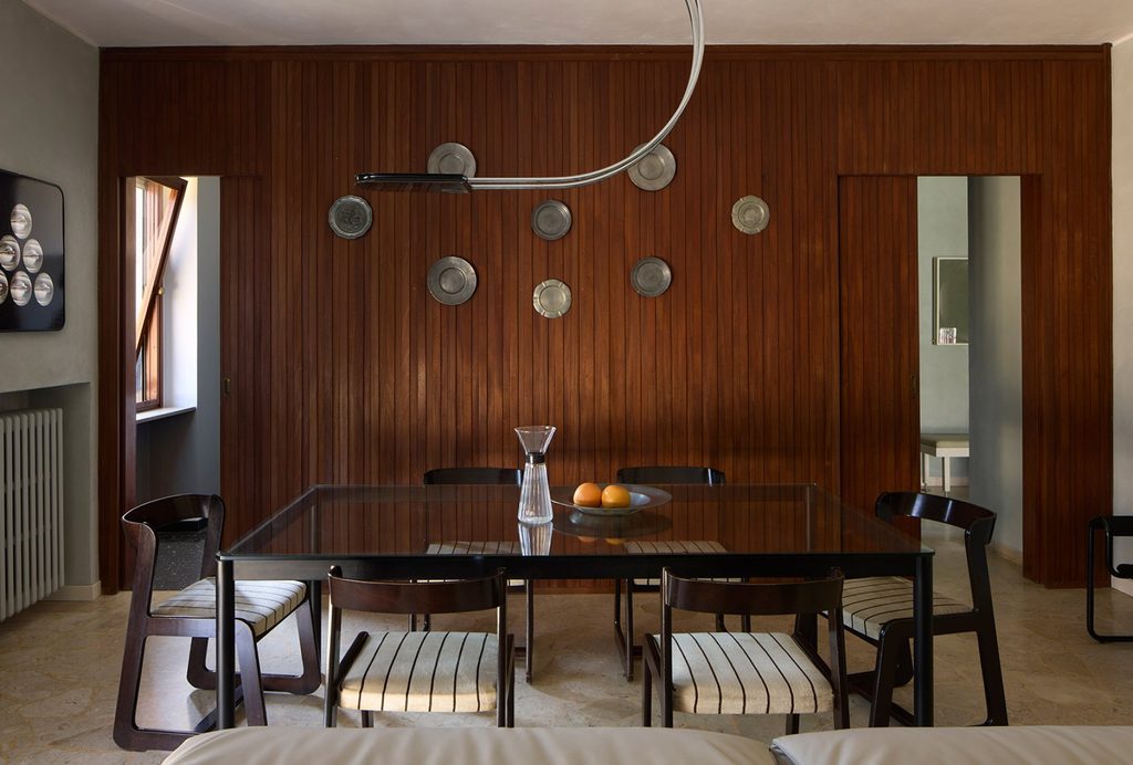 Mid-century modern dining room with dark wood wall paneling, decorative wall plates, and a matching dark wood dining set. top interior design firms in milan