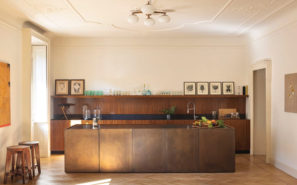 Spacious modern kitchen with a large metallic bronze island, wood-paneled back counter, and classic herringbone parquet flooring.  top interior design firms in milan