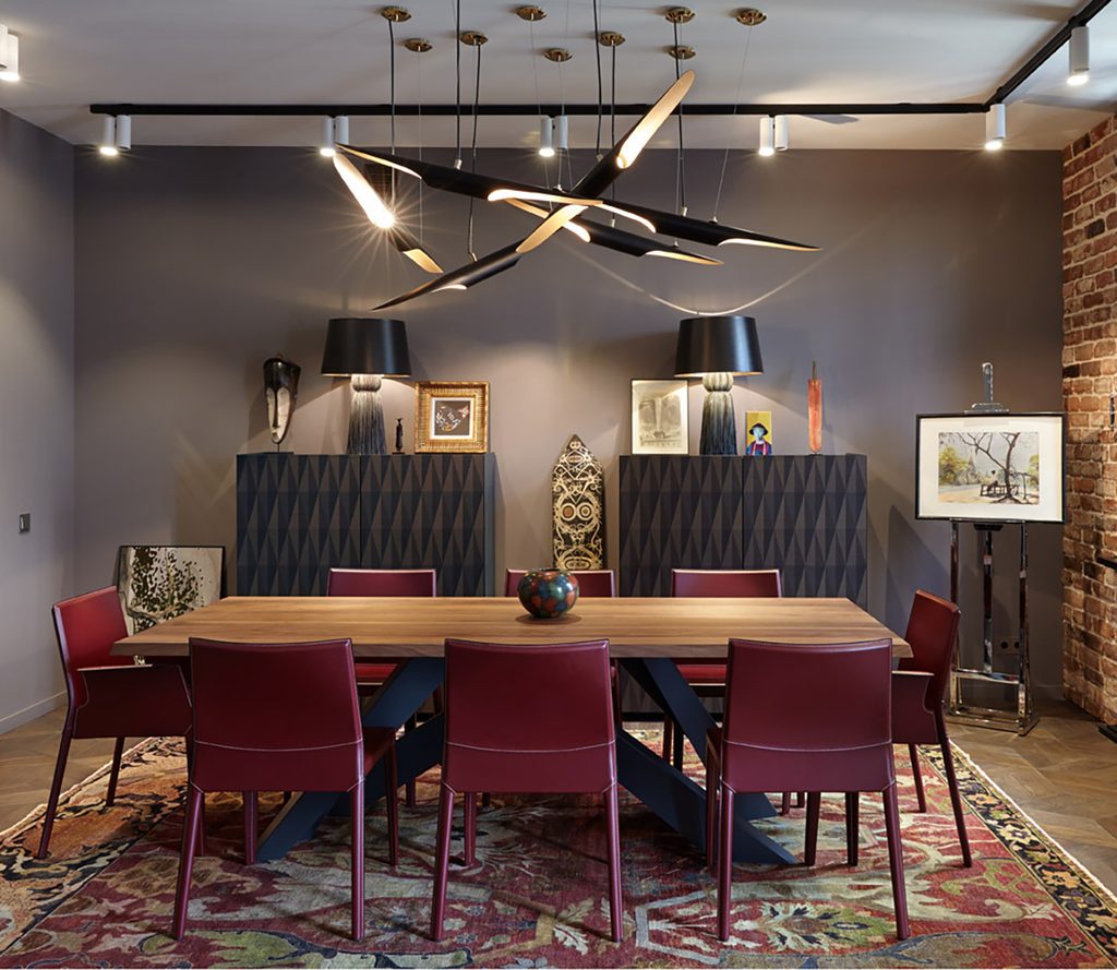 Sophisticated dining room with a wooden table, burgundy upholstered chairs, a modern asymmetric chandelier, and a patterned rug.